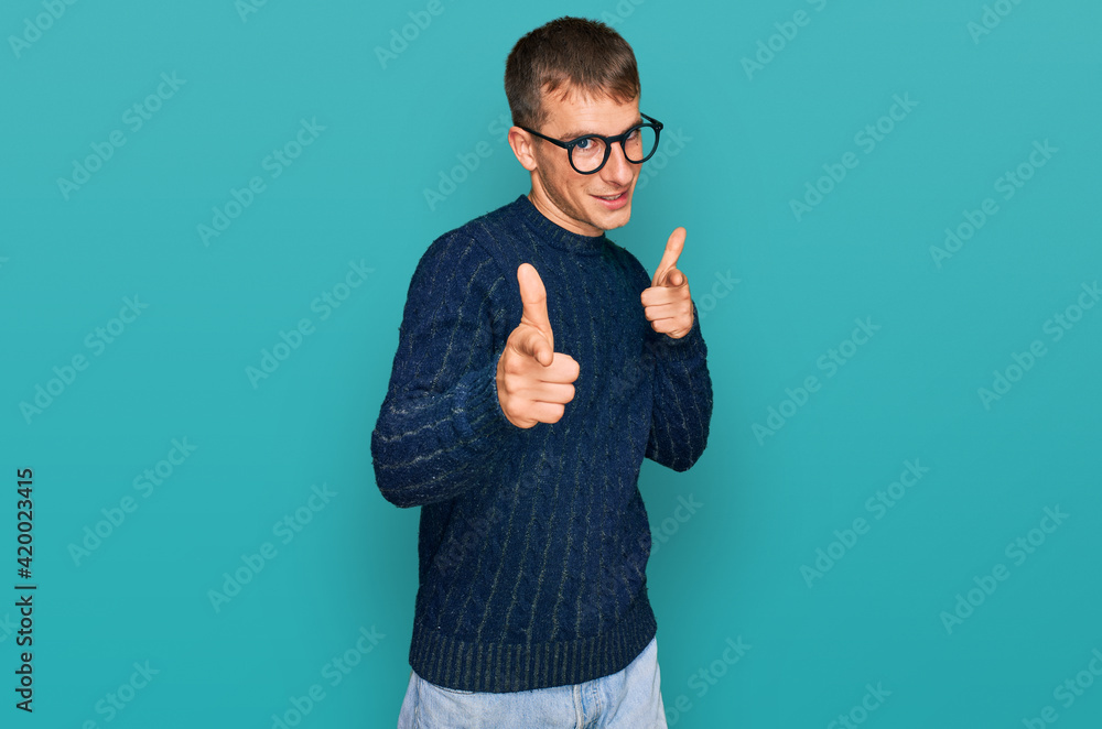 Wall mural young blond man wearing casual clothes and glasses pointing fingers to camera with happy and funny f