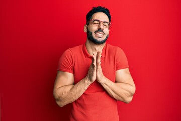 Young hispanic man wearing casual clothes and glasses begging and praying with hands together with hope expression on face very emotional and worried. begging.