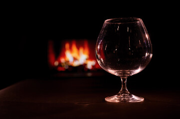 Empty brandy glass on the background of the fireplace in the dark.