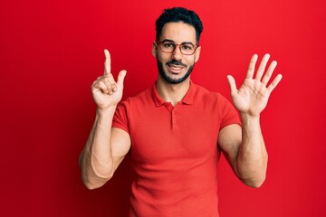 Fototapeta premium Young hispanic man wearing casual clothes and glasses showing and pointing up with fingers number seven while smiling confident and happy.