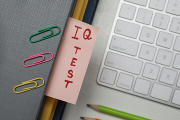 Paper with words IQ Test in notebook, keyboard and fasteners on office table, flat lay
