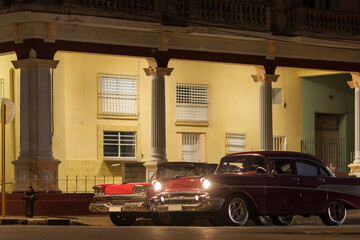 Fototapeta na wymiar Amazing old american car on streets of Havana with colourful buildings in background during the night. Havana, Cuba.