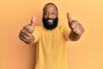 Young african american man wearing casual clothes approving doing positive gesture with hand, thumbs up smiling and happy for success. winner gesture.