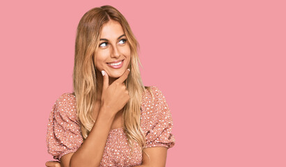 Beautiful blonde young woman wearing summer top with hand on chin thinking about question, pensive expression. smiling with thoughtful face. doubt concept.