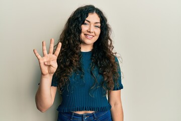 Young brunette woman with curly hair wearing casual clothes showing and pointing up with fingers number four while smiling confident and happy.