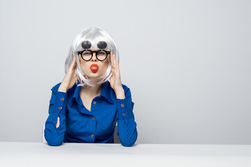 Cheerful Woman in a White wig red lips dark glasses sits at a table in a blue shirt