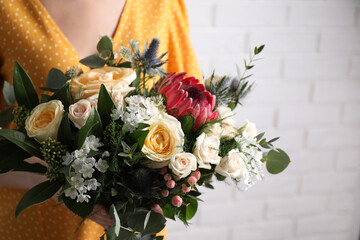 Woman with bouquet of beautiful roses near white brick wall, closeup