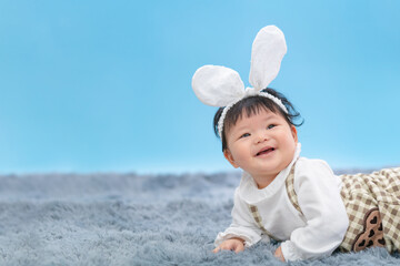 Baby in Easter bunny hairband. Asian happy baby crawling on carpet on blue background. Cute 6 months baby start crawling with copy space as Easter concept, baby or kid department in hospital