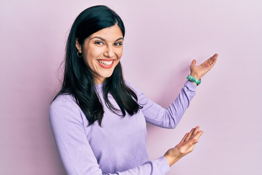 Young hispanic woman wearing casual clothes inviting to enter smiling natural with open hand