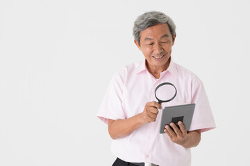 Portrait of a senior older Asian man holding and using magnifier glass to see and watch screen of tablet computer on white background. Idea for older people eyes health problem