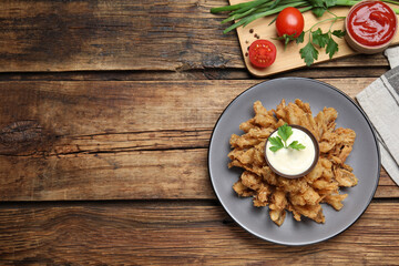 Fried blooming onion with dipping sauce served on wooden table, flat lay. Space for text