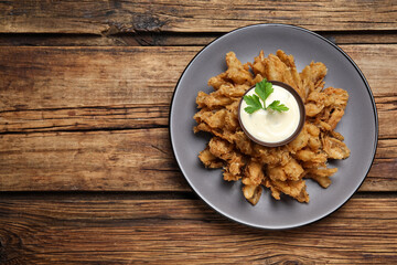 Fried blooming onion with dipping sauce served on wooden table, top view. Space for text