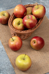 Wicker basket of ripe shiny apples on marble surface