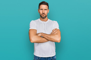 Fototapeta premium Handsome man with beard wearing casual white t shirt skeptic and nervous, disapproving expression on face with crossed arms. negative person.