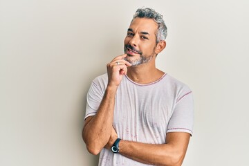 Middle age grey-haired man wearing casual clothes looking confident at the camera with smile with crossed arms and hand raised on chin. thinking positive.