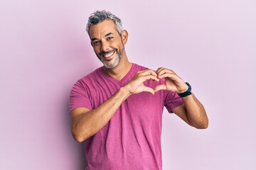 Middle age grey-haired man wearing casual clothes smiling in love showing heart symbol and shape...