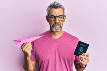 Middle age grey-haired man holding paper plane and passport depressed and worry for distress,...
