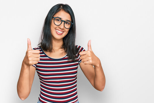 Beautiful asian young woman wearing casual clothes and glasses approving doing positive gesture with hand, thumbs up smiling and happy for success. winner gesture.