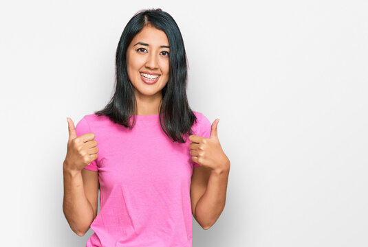 Beautiful asian young woman wearing casual pink t shirt success sign doing positive gesture with hand, thumbs up smiling and happy. cheerful expression and winner gesture.