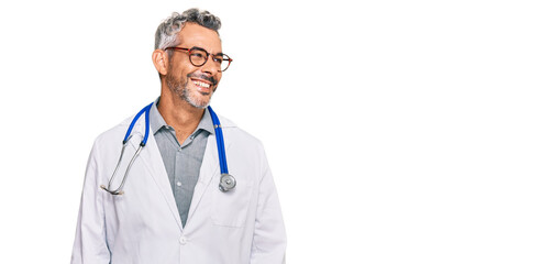 Middle age grey-haired man wearing doctor uniform and stethoscope looking away to side with smile...