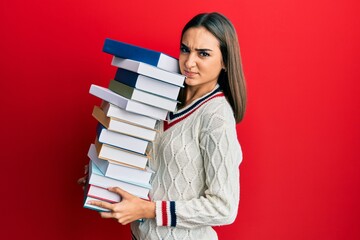 Young brunette student girl holding a pile of books skeptic and nervous, frowning upset because of problem. negative person.
