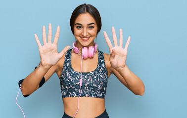 Beautiful brunette woman wearing gym clothes and using headphones showing and pointing up with...