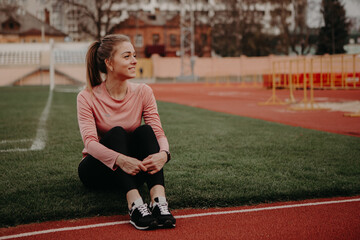 A girl sits on the corner of a football field, looks at the camera and smiles. Sporty woman in...