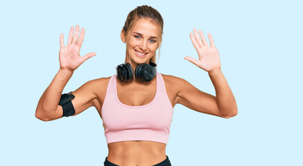 Young blonde woman wearing gym clothes and using headphones showing and pointing up with fingers number ten while smiling confident and happy.
