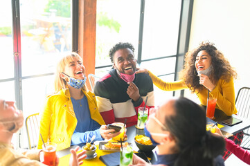 Happy friends having genuine fun drinking cocktail at bar with open face mask - New normal lifestyle concept with happy people laughing together at restaurant