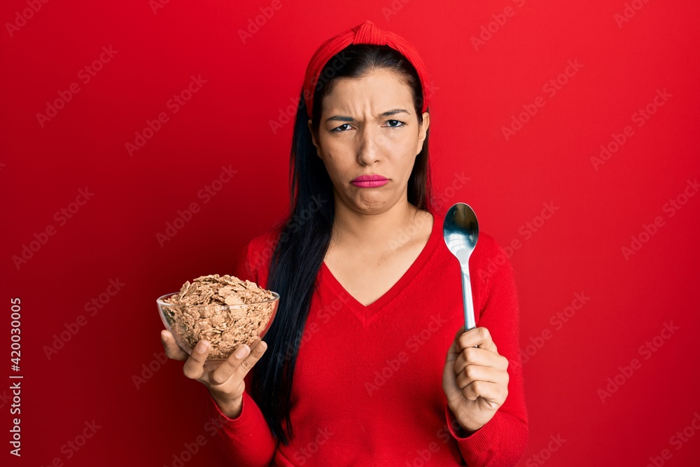 Sticker young latin woman holding cornflakes and spoon skeptic and nervous, frowning upset because of proble