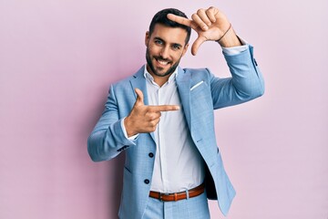 Young hispanic businessman wearing business jacket smiling making frame with hands and fingers with...