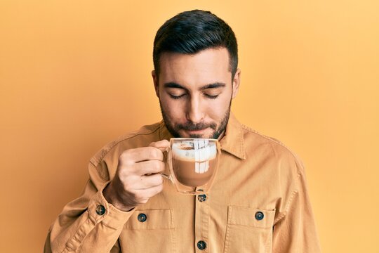 Handsome hispanic man enjoying a cup of coffee over yellow background