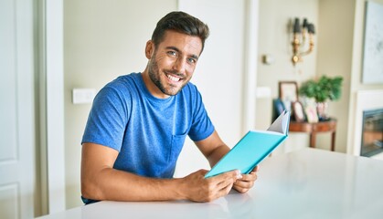 Young handsome man smiling happy reading book at home