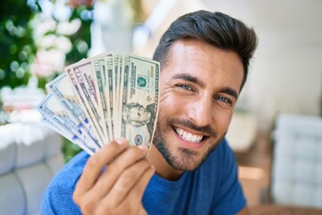 Young hispanic man smiling happy holding american dollars at the terrace.