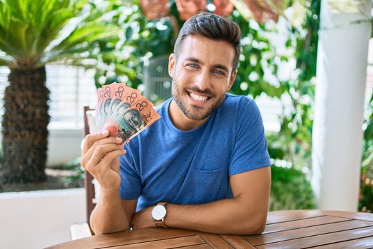 Young hispanic man smiling happy holding australian dollars banknotes at the terrace.
