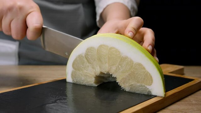 Female hands cut slice of pomelo on cutting board. Close up, 150 fps