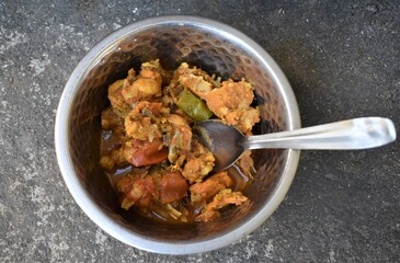 Homemade Masala Chicken curry  with tomato and spices in a silver bowl with spoon.
