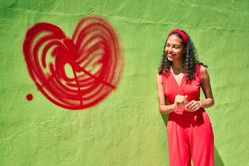 Young african american girl smiling happy leaning on the wall with heart graffiti at city.