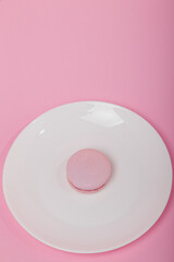 One pink macaroon on white plate on pink paper background. Sweet bakery, copy space. Overweight, diet, diabetes, healthy eating habits. Vertical
