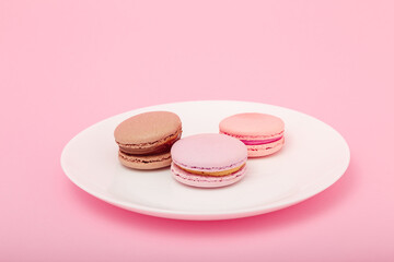 three macaroons on white plate on pink paper background. Sweet bakery, copy space. Overweight, diet, diabetes, healthy eating habits.