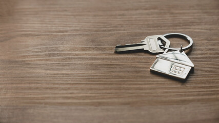 Real estate or property concept. Selective focus of key and house keychain on wooden background with copy space.