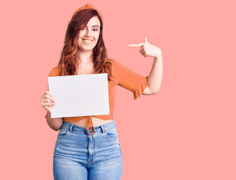 Young beautiful woman holding cardboard banner with blank space pointing finger to one self smiling happy and proud