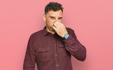 Young hispanic man wearing casual clothes smelling something stinky and disgusting, intolerable...