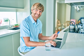 Young irish man using credit card and laptop to buy sitting on the table at home.