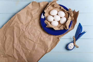 Eggs on paper and blue plate. Easter bunny made from egg and polka dot napkin ears on wooden blue background. Easter concept. Top view, copy space.