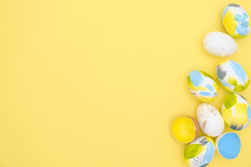 Top view of easter holiday yellow backdrop with creative eggs decorations in trendy blue, gray, golden colors. Flat lay colorful composition with copy-paste for text for postcard, banner, invitation