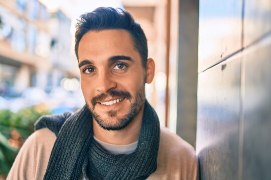 Young hispanic man smiling happy wearing scarf leaning on the wall at the city.