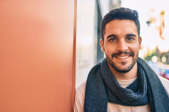 Young hispanic man smiling happy wearing scarf leaning on the wall at the city