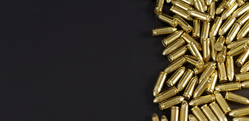 Many brass gun bullets on black table closeup view from above, space for text left side - obrazy, fototapety, plakaty
