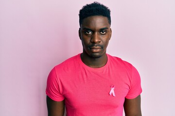 Handsome black man wearing pink cancer ribbon attached on shirt thinking attitude and sober...
